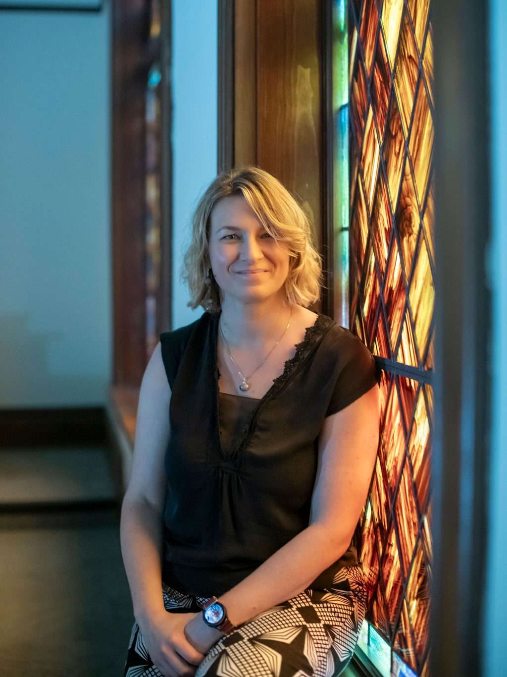 Natalie Chwalisz rests on a windowsill of a stained glass window.